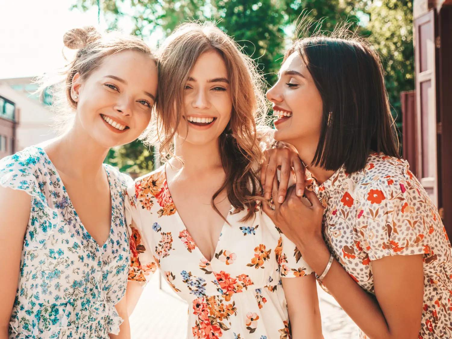 Trzy młode kobiety w kwiecistych sukienkach uśmiechają się i śmieją razem na świeżym powietrzu w słoneczny dzień. tarasy szczecin