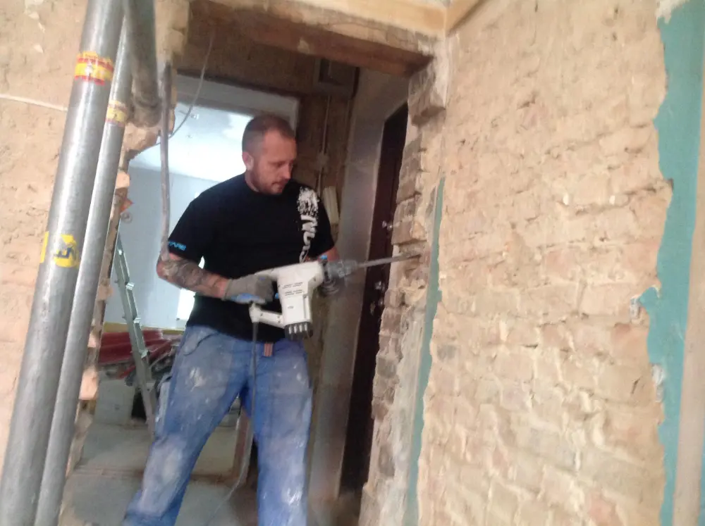 Mężczyzna w ubraniu roboczym używa elektronarzędzia do przecięcia ceglanej ściany wewnątrz remontowanego budynku. tarasy szczecin