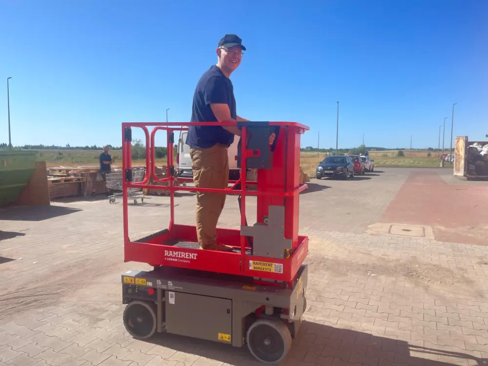 Osoba stojąca na małej czerwonej ruchomej windzie na zewnątrz w słoneczny dzień, uśmiechająca się do kamery. tarasy szczecin