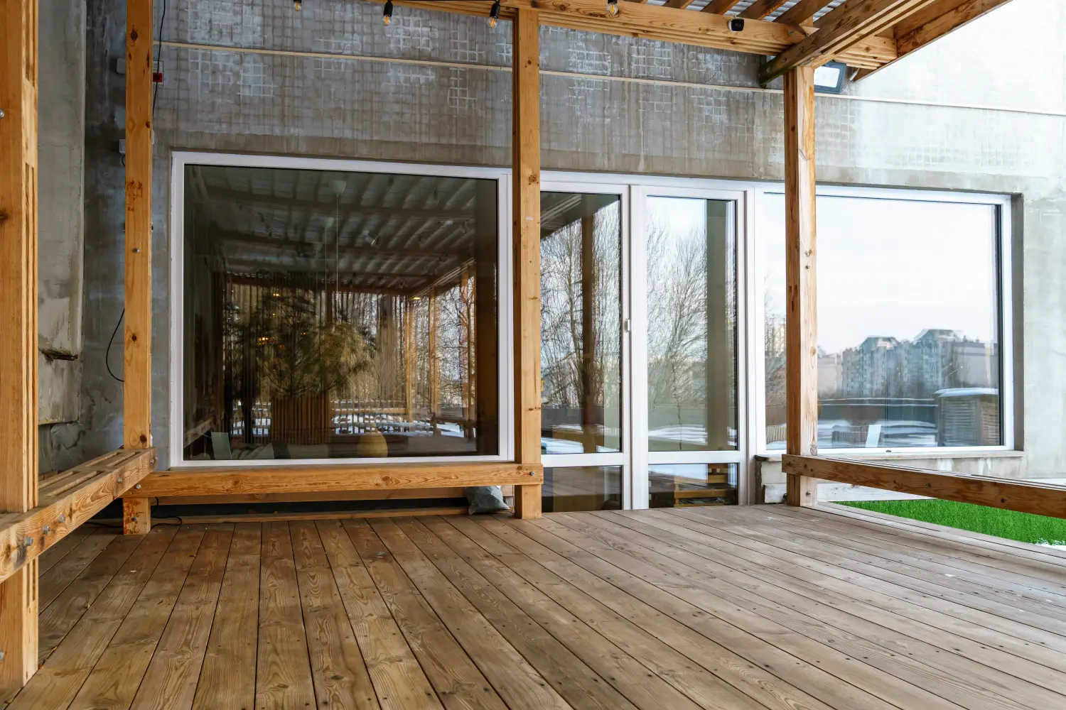Drewniane patio z dużymi szklanymi oknami i drzwiami, odbijające drzewa i budynki na zewnątrz. tarasy szczecin